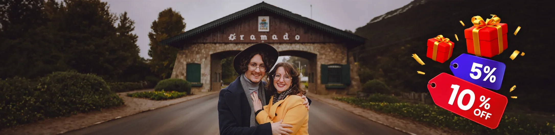 Andy e PH abraçados em frente ao pórtico de Gramado, com etiquetas de 5% e 10% de desconto
